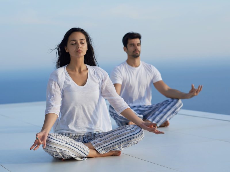 young couple practicing yoga at sunset in modern home terace with ocean and sunset in background