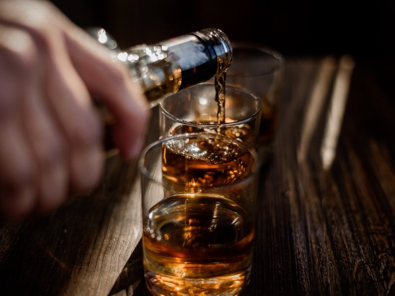 Pouring strong alcohol drink into the glasses which are on the wooden table