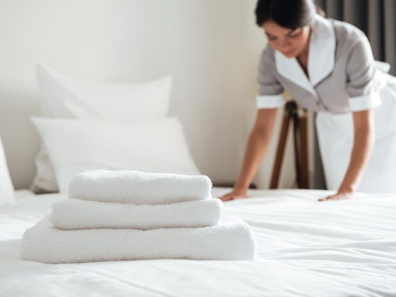 Young hotel maid making the bed with clean fresh towels